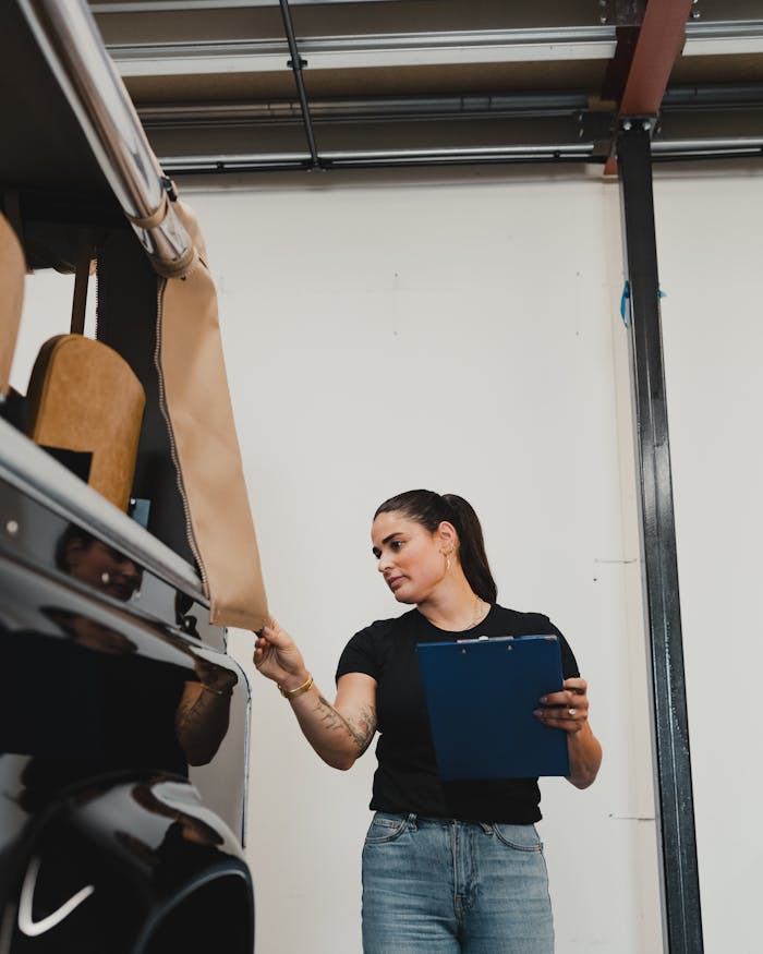 Female mechanic in a workshop checking vehicle interior with clipboard. Professional car maintenance service.